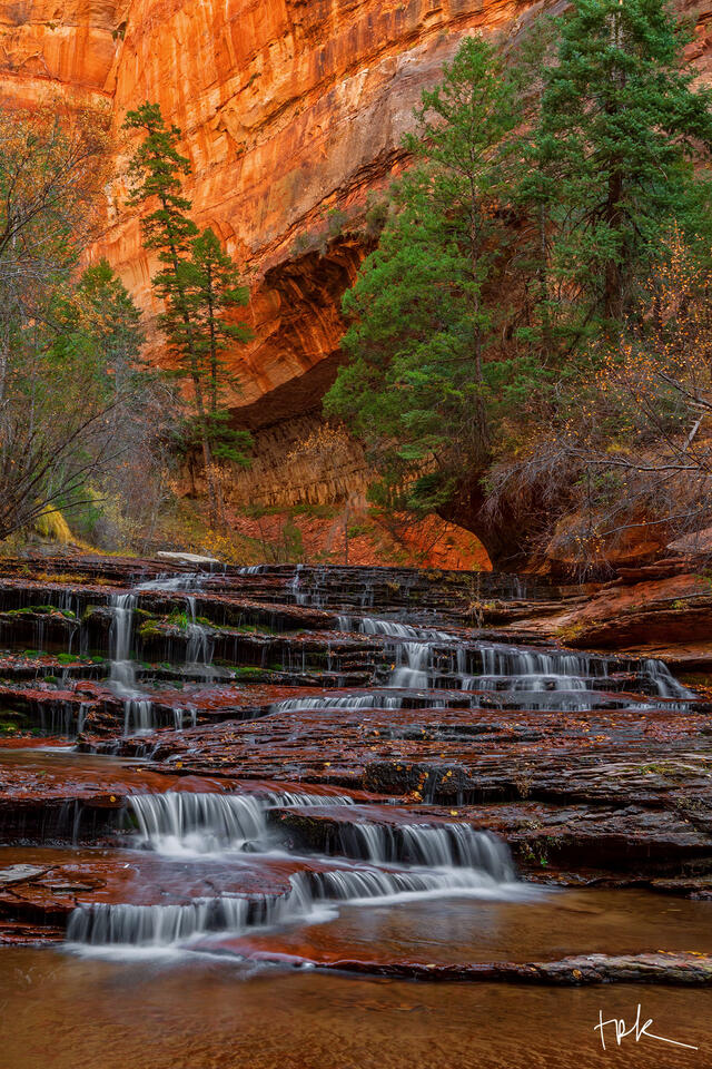 Limited edition print of a Utah waterfall descending down layers of red rock underneath orange-colored sandstone canyon walls.