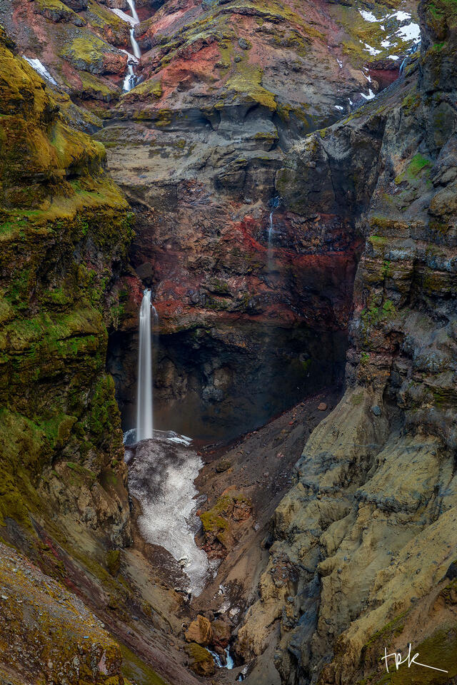 Limited edition print of a tall, thin waterfall at the end of an Icelandic canyon made of colorful rock.