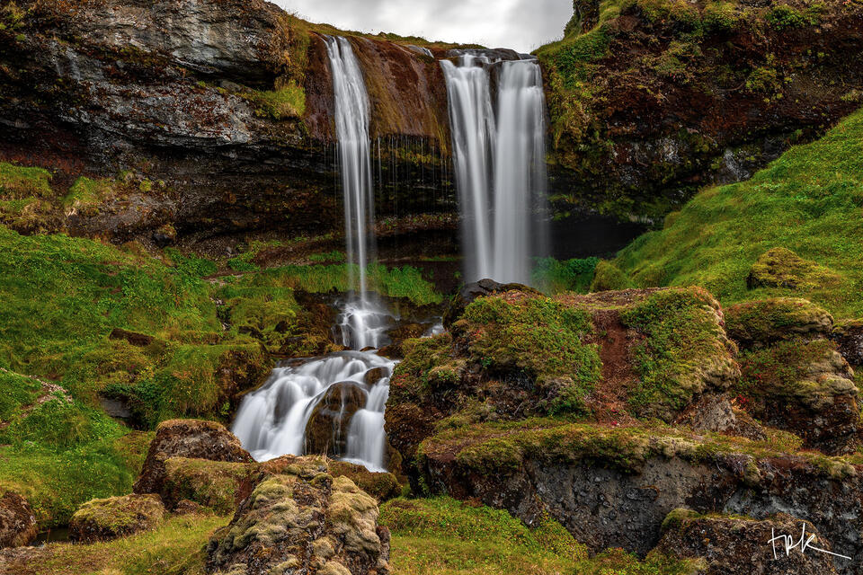 Limited edition print of an Icelandic waterfall pouring over a ledge and tumbling downstream over rocks surrounded by green grass.