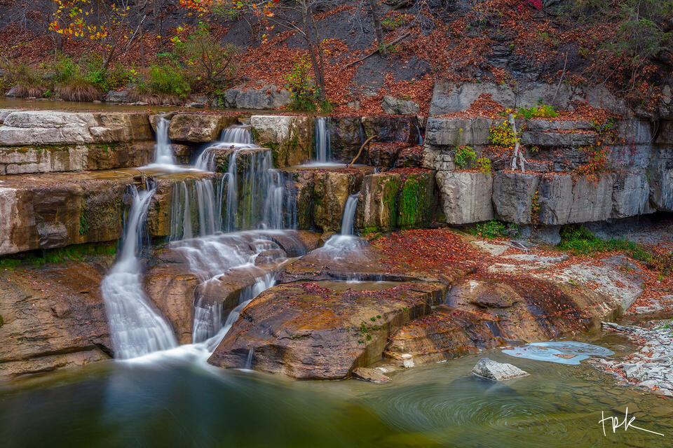 Limited edition print of a waterfall progressing down a series of steps to a green-colored plunge pool in the New York woodland in fall.