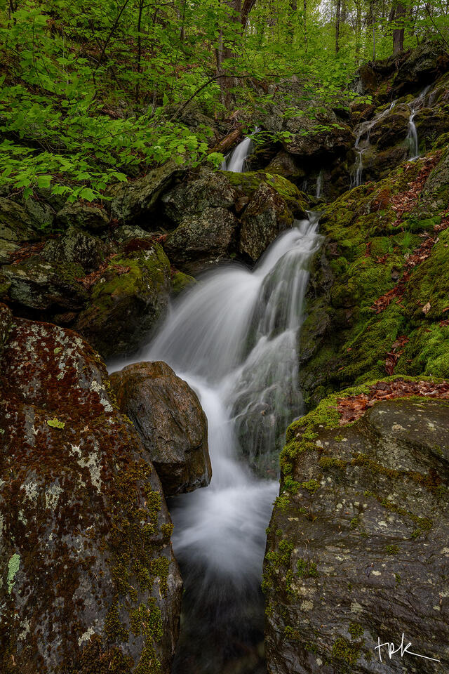 Limited edition print of a small Connecticut woodland waterfall as viewed from downstream between two large boulders.