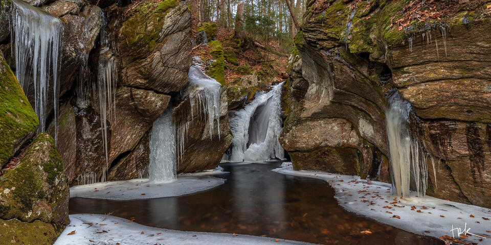 Limited edition panoramic print of a chasm in the Connecticut woodland with an ice-covered waterfall at the back and columns of ice and icicles on either side.